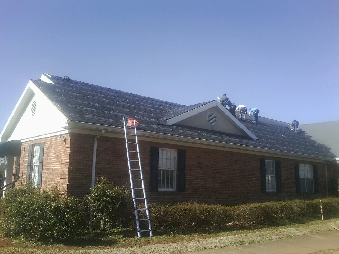 Crew tearing shingles off a brick ranch roof with a ladder set — Emergency Roof Repair work by our crew in Jacksonville Beach
