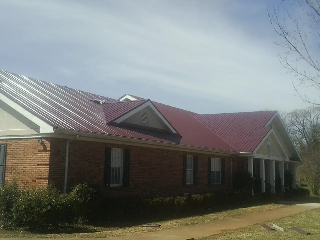 Red metal roof with gabled entries on a long brick building, from a Hail Damage Roof Repair job in Jacksonville Beach