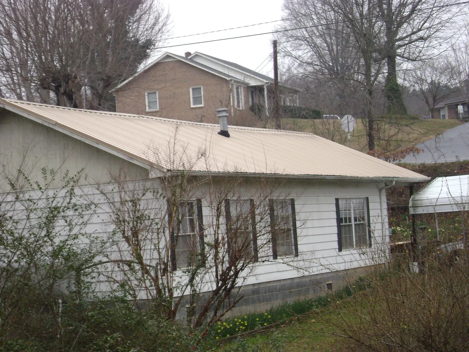 Tan metal roof on a white sided house set into a hillside — Commercial Roofing by Roofing Brothers in Jacksonville Beach