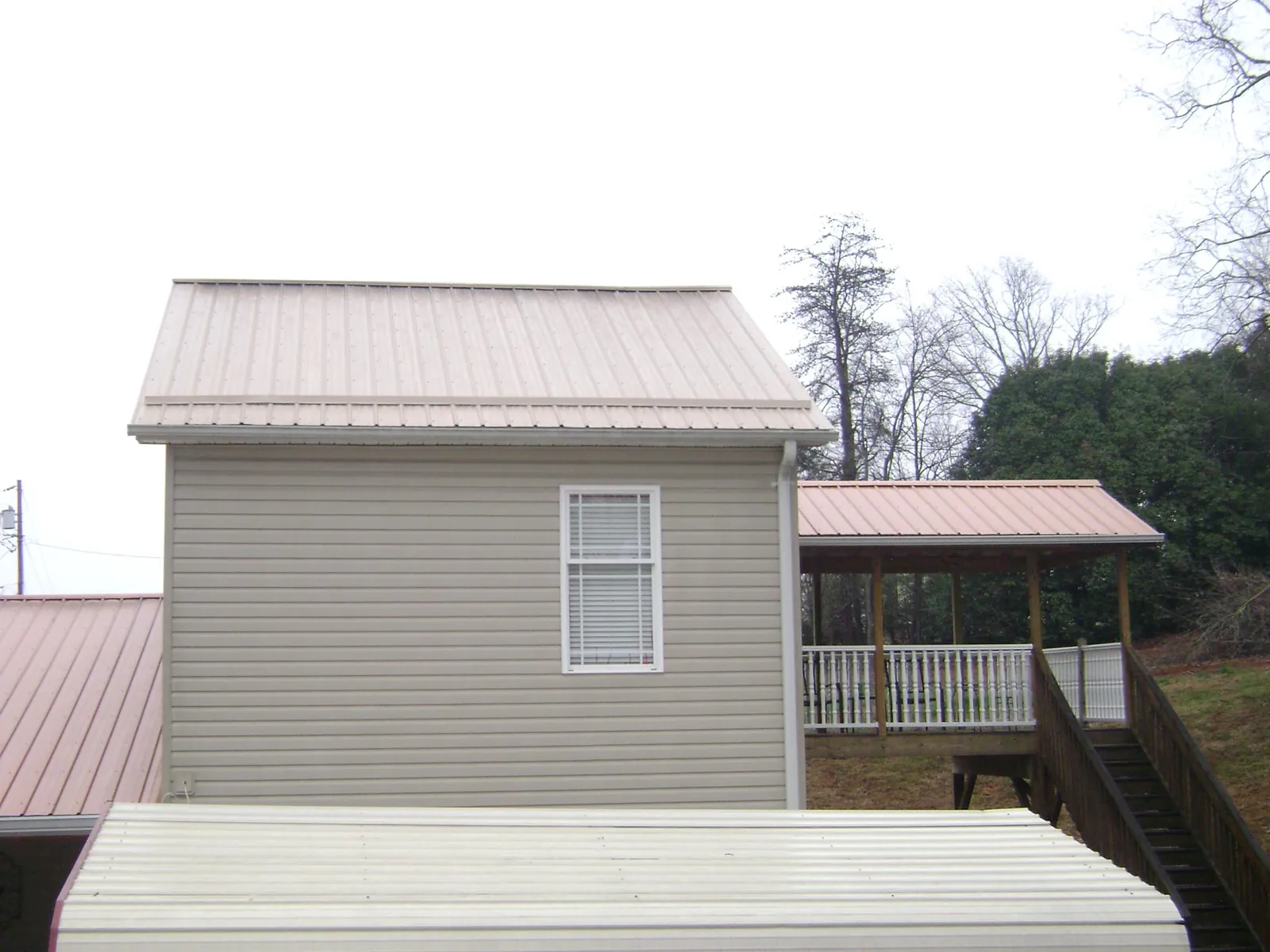 Tan metal roofs on a two story addition and attached porch, from a Roof Replacement job in Jacksonville Beach